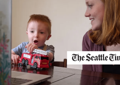Child playing with a red train while a woman looks at him smiling. The Seattle Times.