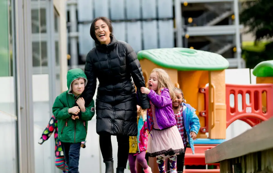 A woman holds hands with a girl and a boy outdoors wearing winter coats.