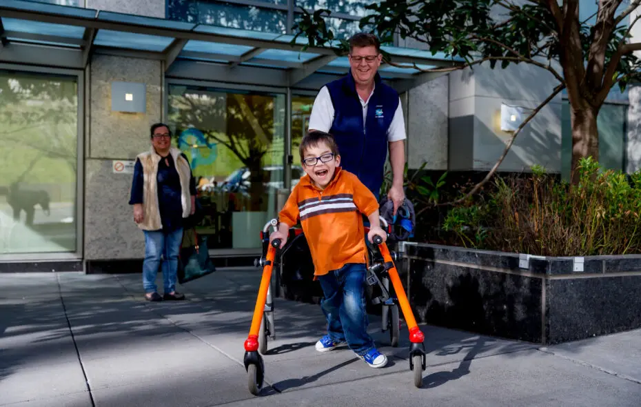 A boy using a walker and a man stand outdoors.