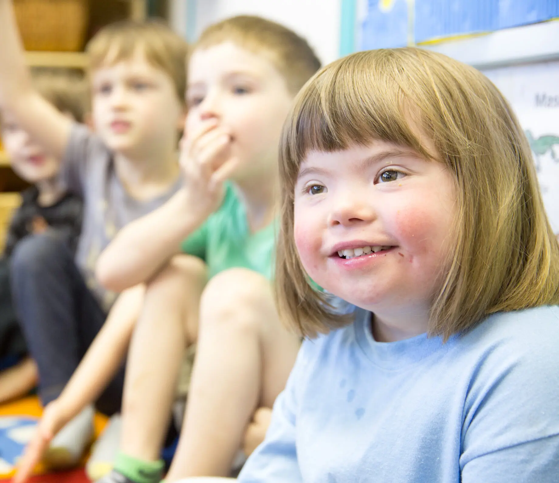 A close up of a girl with Down's Syndrome sitting on the floor with her classmates during circle time.