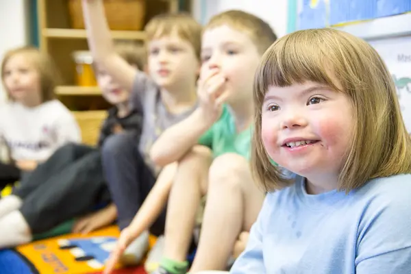 Young children in a classroom sitting on the floor smiling.