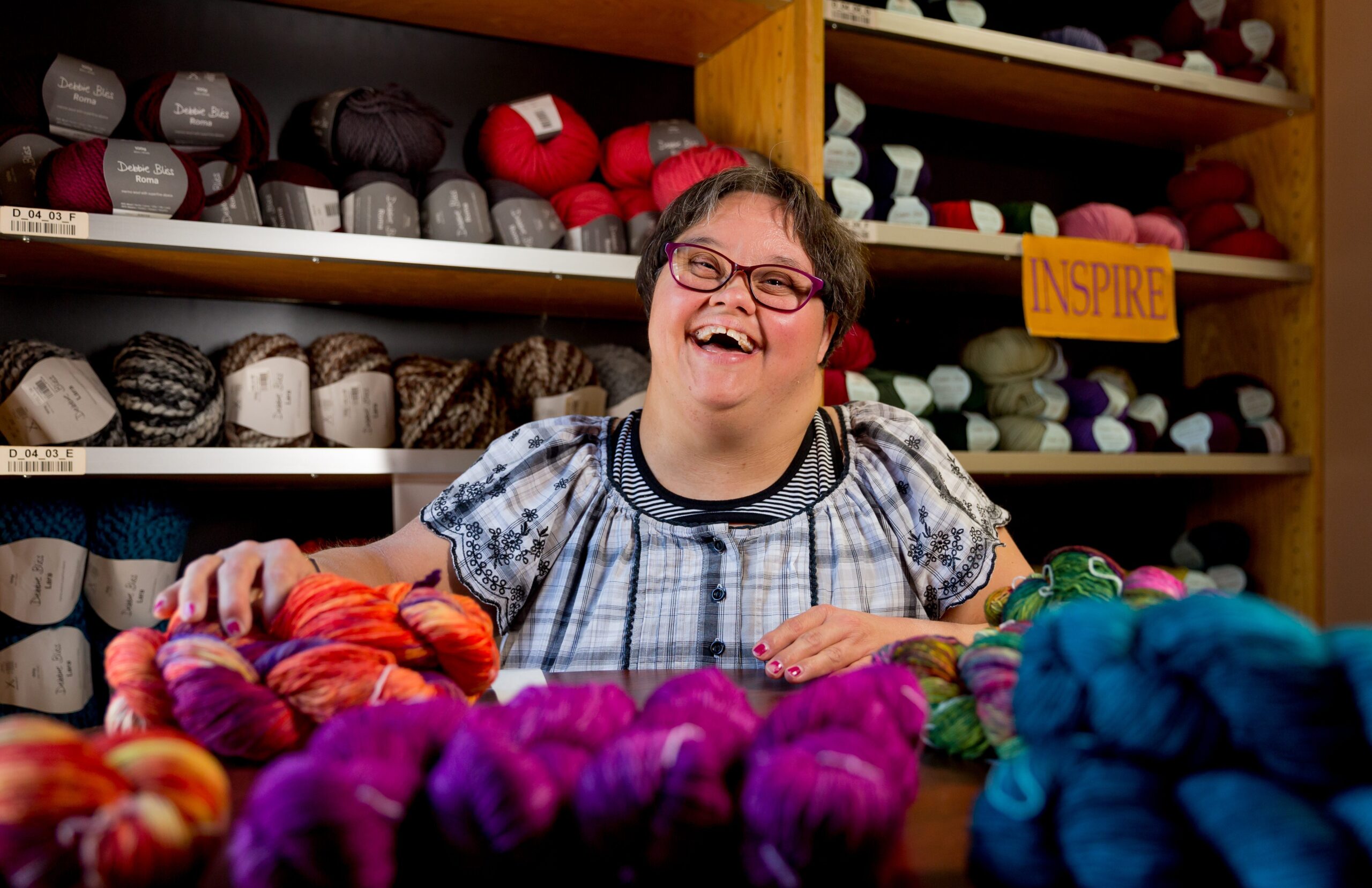 Smiling developmentally disabled adult woman with balls of yarn in a shop.