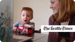 Child playing with a red train while a woman looks at him smiling. The Seattle Times.