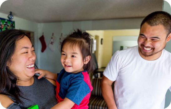 Mother holding a child, and father smiling next to them.